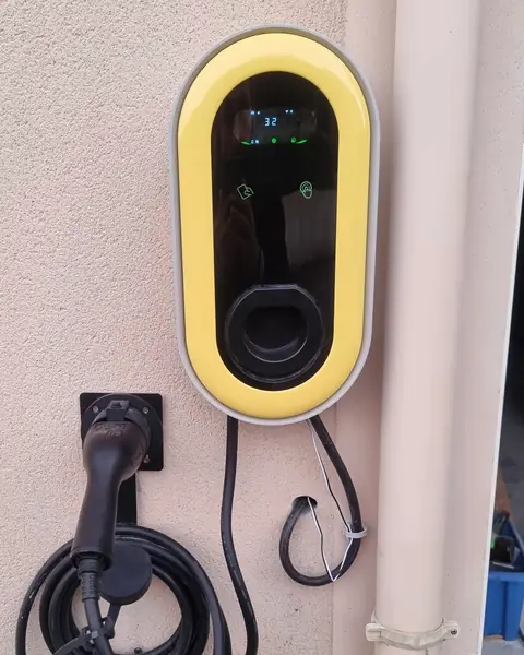 Borne de recharge murale à cadre jaune posée sur une façade beige, câble enroulé sur son support