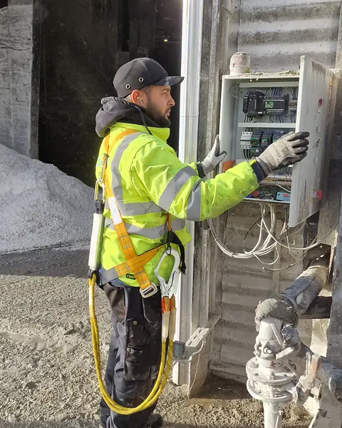 Technicien d’Ave Green de profil, en veste haute visibilité et harnais, qui ouvre une armoire électrique fixée sur un bardage métallique