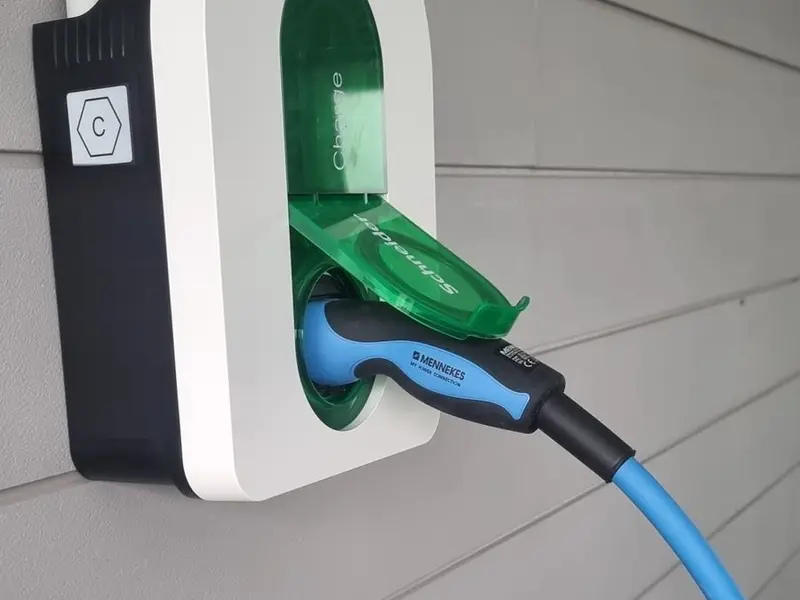 Câble de recharge bleu branché dans la prise Type 2 d’une borne murale, clapet vert ouvert, sur un bardage gris