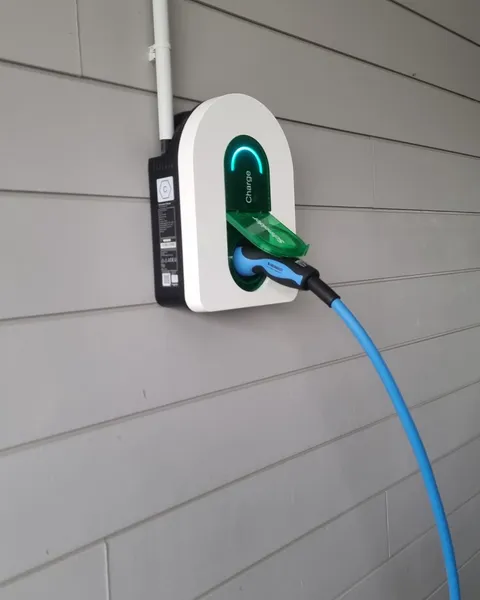 Borne de recharge Schneider Charge posée sur le bardage gris clair d’une maison, clapet vert ouvert, câble bleu branché