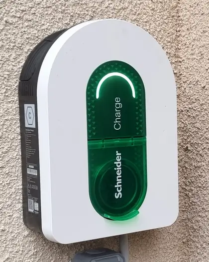 Une borne de recharge Schneider Charge posée sur un mur crépi, vue de face : arche blanche, bande verte « Charge » et son arc lumineux allumé.
