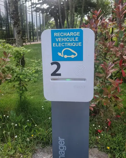 Borne de recharge sur pied numérotée 2, voyant vert allumé, devant des massifs