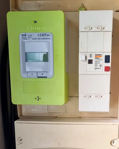 Compteur Linky vert et, à côté, le boîtier blanc du disjoncteur de branchement, dans une niche technique