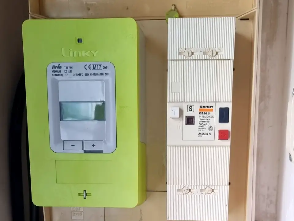 Compteur Linky vert et, à côté, le boîtier blanc du disjoncteur de branchement, dans une niche technique