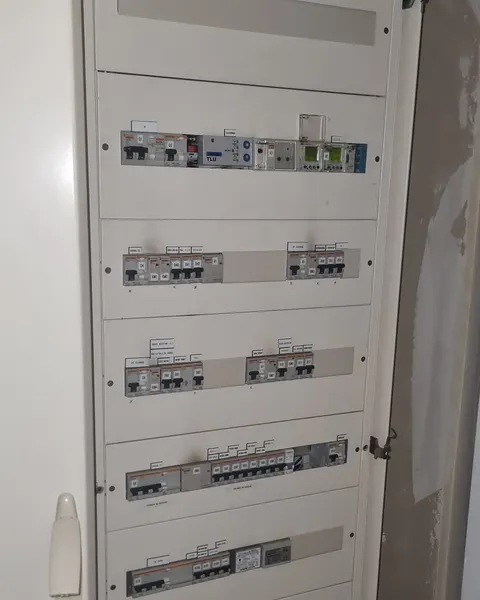 Armoire électrique ouverte dans un local technique, rangées de disjoncteurs étiquetés