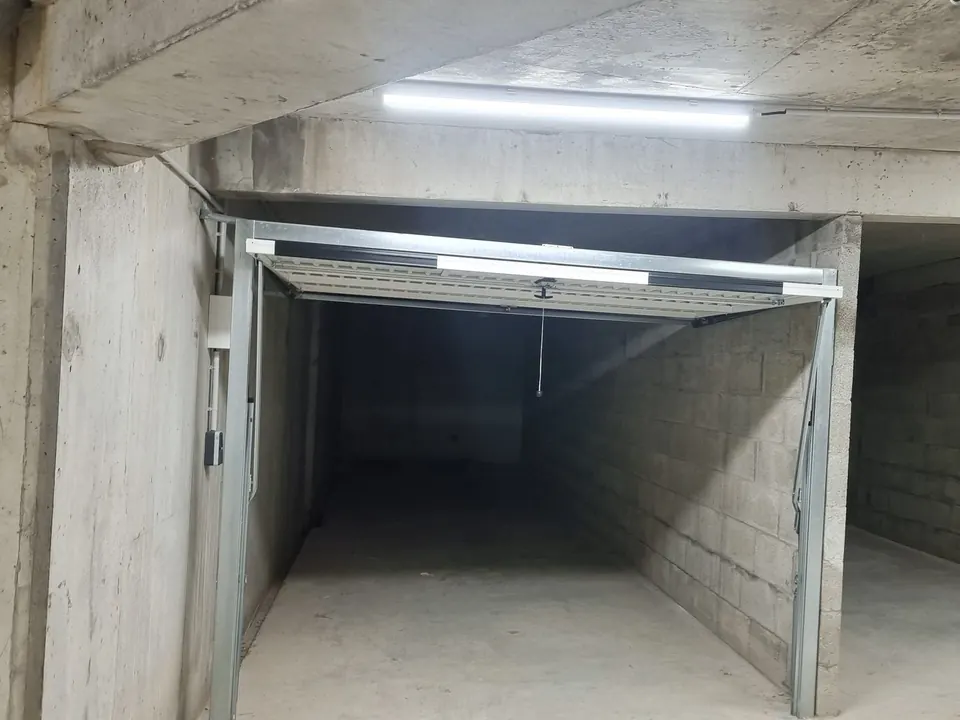 Parking souterrain de résidence : box à porte basculante ouvert, murs en parpaings, éclairage au plafond
