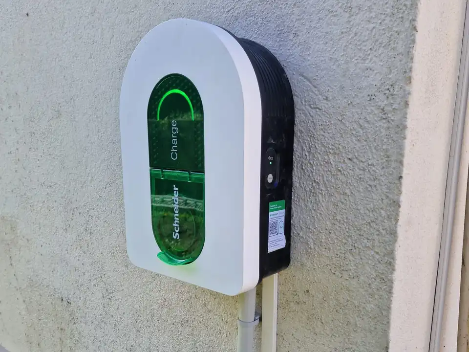 Borne de recharge murale blanche et noire, trappe verte translucide allumée, fixée sur un mur crépi clair