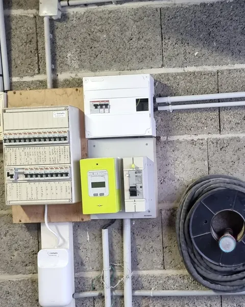 Compteur Linky vert et disjoncteur de branchement entre un tableau électrique et un nouveau coffret blanc, sur un mur en parpaings