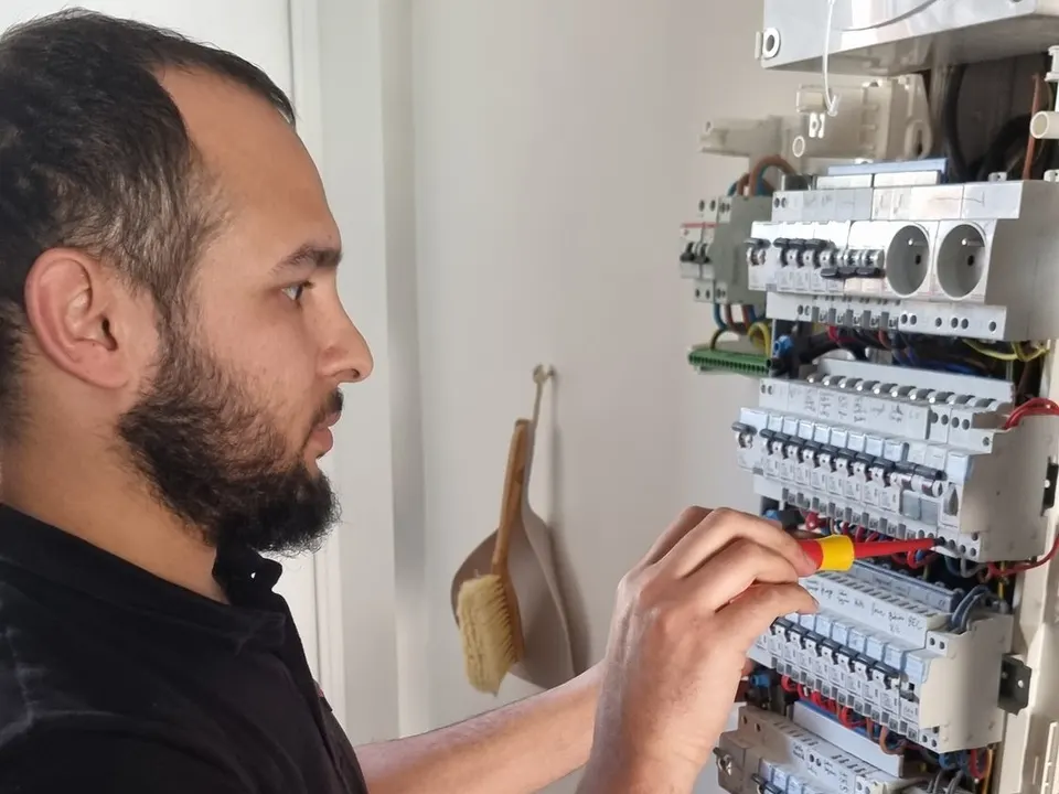 Électricien en polo noir qui serre au tournevis isolé les disjoncteurs d’un tableau électrique ouvert