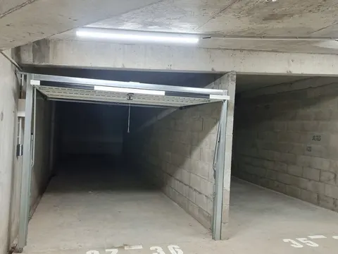 Parking souterrain d’une résidence : box en béton à porte basculante ouverte, places numérotées au sol