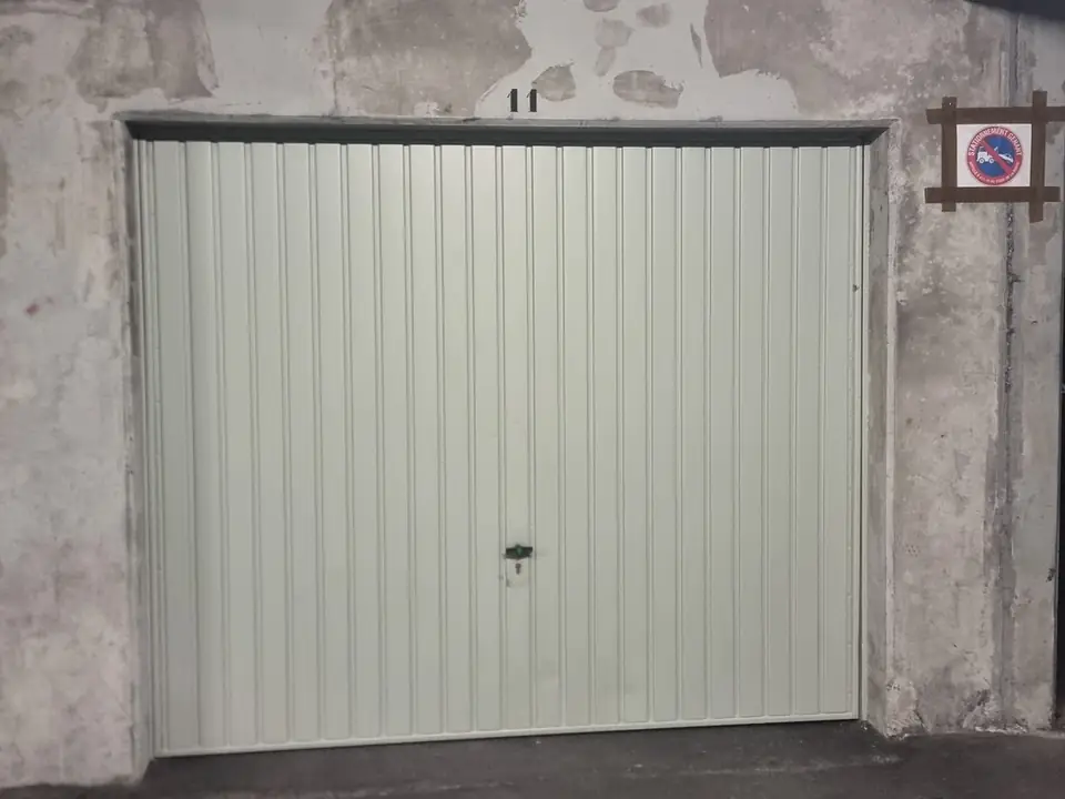 Sous-sol d’une résidence : porte de box basculante fermée, numéro 11 peint au-dessus, mur en béton écaillé