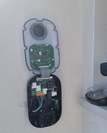 Borne Wallbox ouverte pendant la pose sur un mur crépi blanc : cartes électroniques et prise visibles