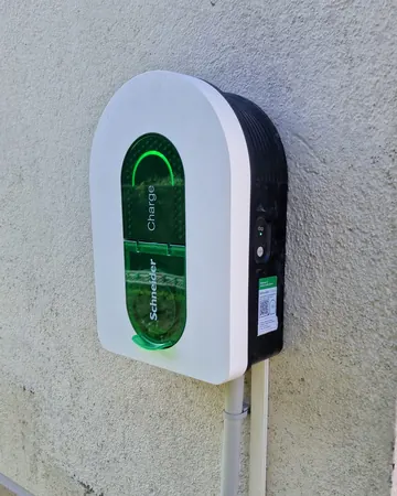 Borne Schneider Charge blanche et noire vue de trois quarts, trappe verte et arc lumineux vert allumés, sur un mur crépi clair