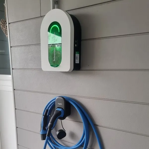 Une borne Schneider Charge allumée sur un bardage gris clair, son câble bleu enroulé sur un support juste en dessous
