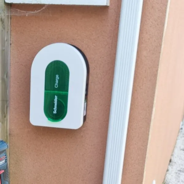 Une borne Schneider Charge blanche à vitre verte posée sur un mur saumon, à côté d’une descente d’eau blanche