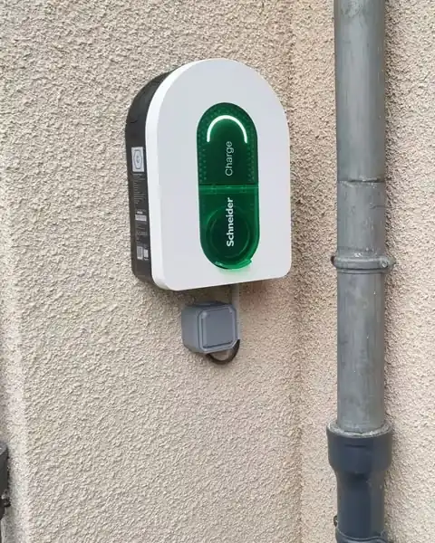 Borne Schneider Charge blanche à voyant vert sur une façade crépie beige, à côté d’une descente pluviale