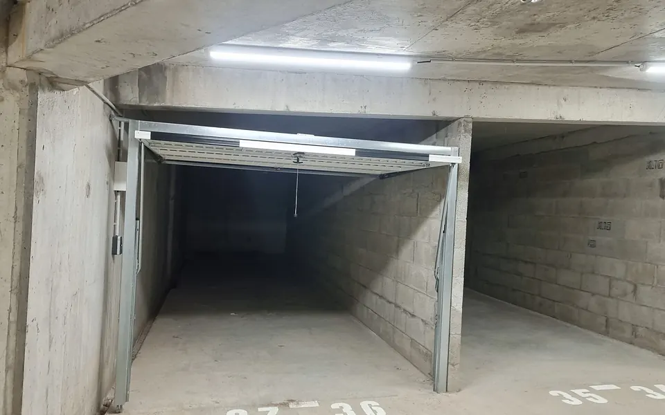 Parking souterrain en béton, box à porte basculante ouverte et numéros de places peints au sol