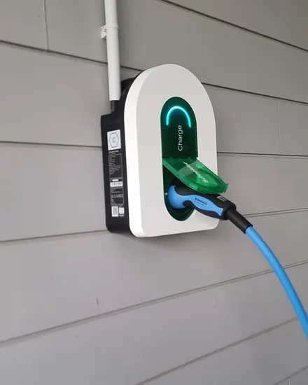 Borne Schneider Charge blanche sur un bardage gris, clapet vert ouvert, câble de recharge bleu branché