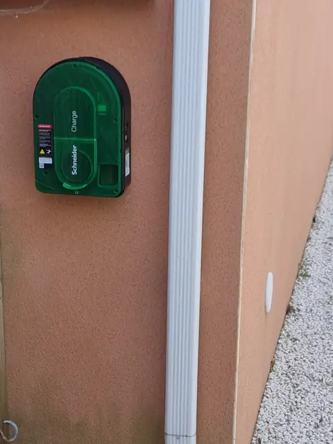Même mur : la borne avec son capot intérieur vert marqué Schneider Charge, à côté de la descente d’eau.