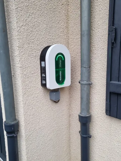 Borne Schneider Charge centrée entre deux descentes d’eau, voyant vert, crépi beige.