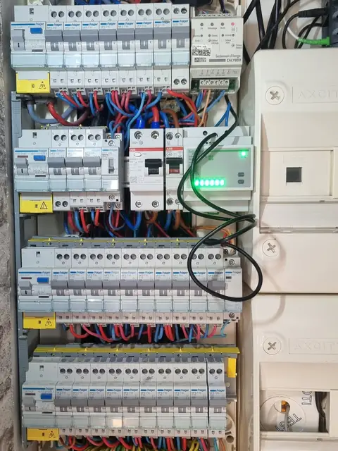 Tableau électrique ouvert à rangées de disjoncteurs, avec un gestionnaire d’énergie et un module à voyants verts.