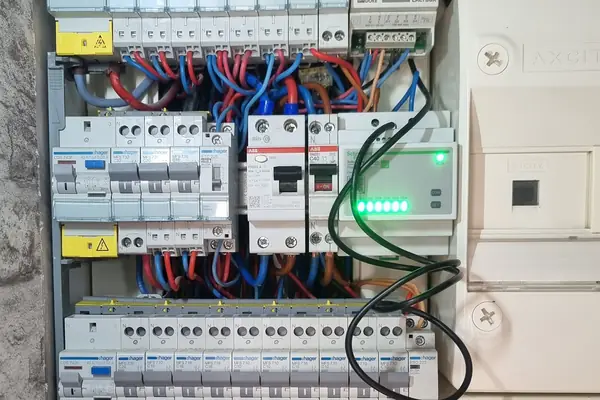 Tableau électrique ouvert : rangées de disjoncteurs, protections différentielles et gestionnaire d’énergie à voyants verts