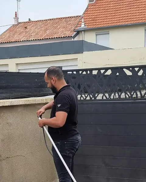 Technicien d’Ave Green tirant un câble dans un tube le long d’un muret, devant un portail gris