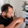 Le technicien d’Ave Green, en polo noir, serre un disjoncteur au tournevis isolé dans un tableau électrique ouvert
