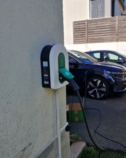 Borne Schneider Charge posée à l’angle d’une façade crépie, câble branché sur une voiture électrique bleu nuit en charge dans l’allée