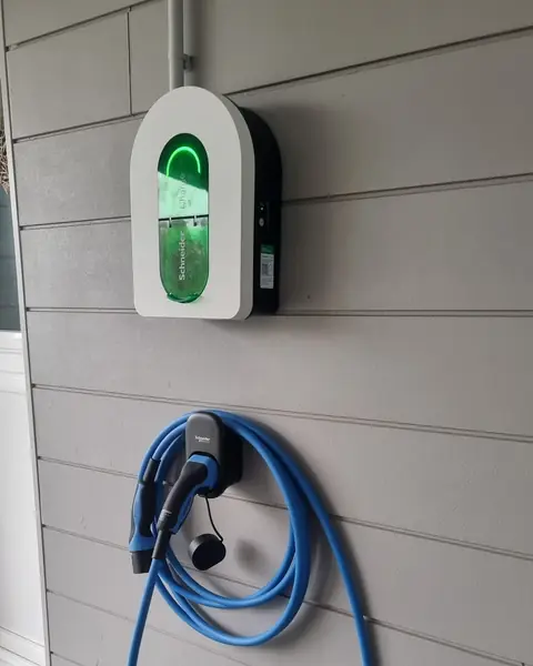 Borne Schneider Charge blanche à voyant vert sur un bardage gris clair, câble de recharge bleu enroulé sur son support