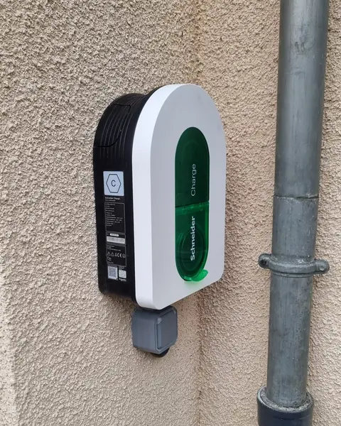 Borne Schneider Charge blanche et noire à capot vert, posée sur un mur crépi beige, à côté d’une descente d’eau